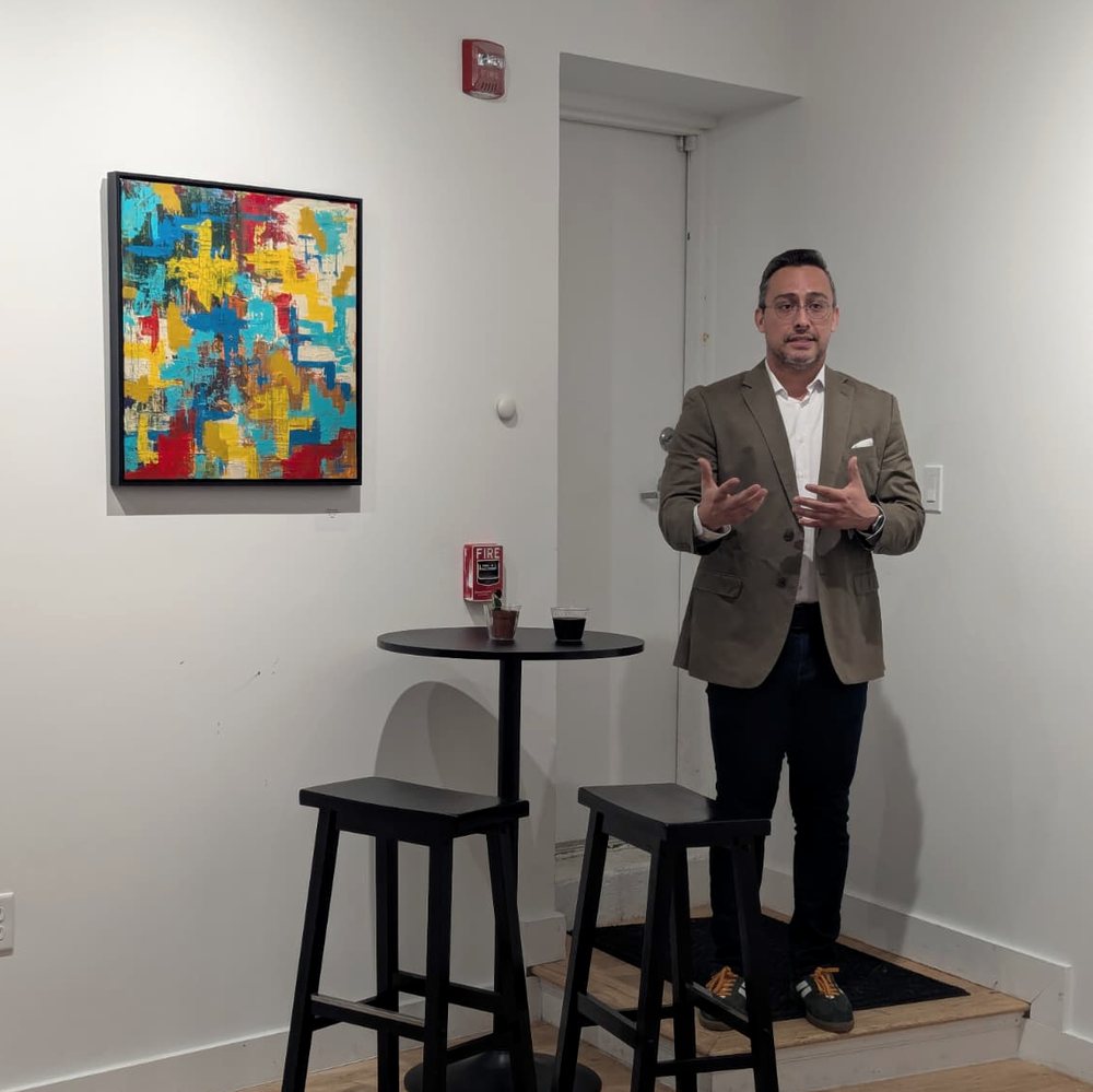 Edward Rocha speaking in a gallery beside one of his abstract paintings